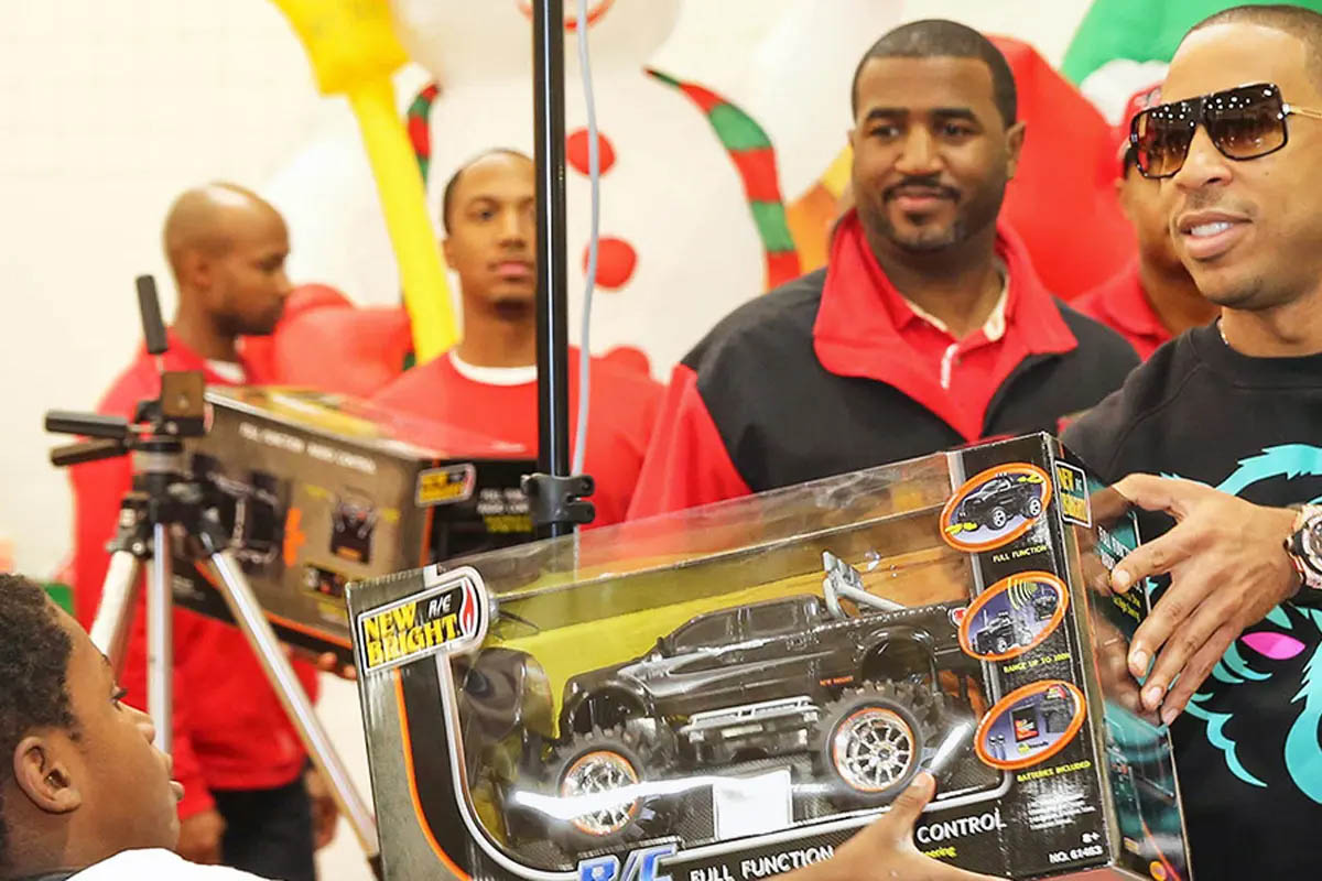 Ludacris hands a new toy truck to a young boy.