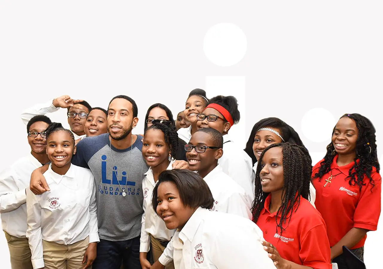 Chris 'Ludacris' Bridges stands with a group of youth wearing white or red shirts. The image is on a white background.