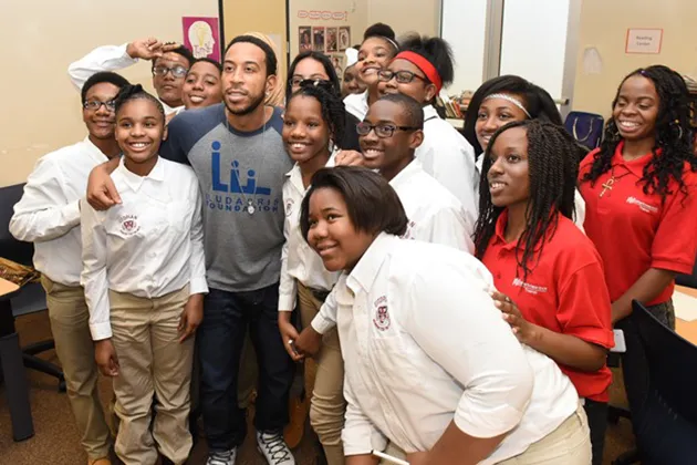 Chris 'Ludacris' Bridges stands with a group of youth wearing white or red shirts.