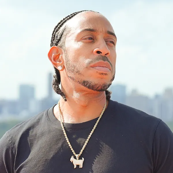 Chris 'Ludacris' Bridges stands with his arms folded. He's wearing a black tank top and a gold chain.